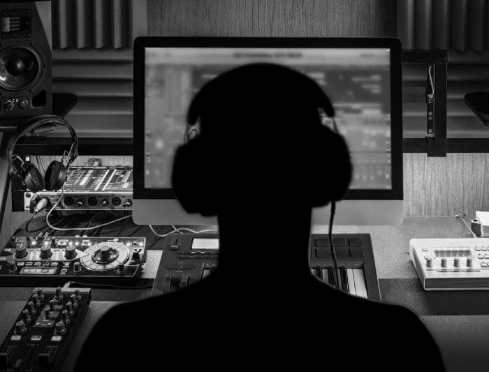 A silhouette of a person with headphones in front of a computer.